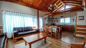 A cozy living room with a sofa, wooden coffee table, and dining area with chairs and a table. A kitchen is visible in the background. - Apartamentos Catedral inn (San Carlos de Bariloche)