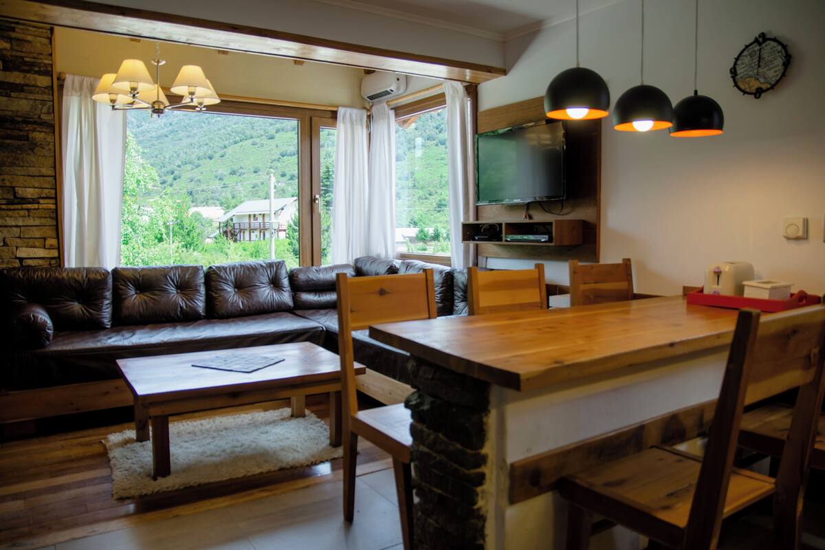 Ein gemütliches Wohnzimmer mit einer Ledersofa, einem Holzessttisch und einem an der Wand befestigten Fernseher.