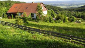 A house with a red roof, surrounded by lush greenery and a wooden fence. - Apartment Pavla With 3 Bedrooms and 1 Bathrooms (Jachymov)