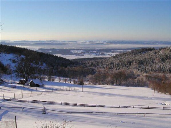 Un paysage enneigé avec une clôture en bois, une petite cabane et une colline boisée en arrière-plan.