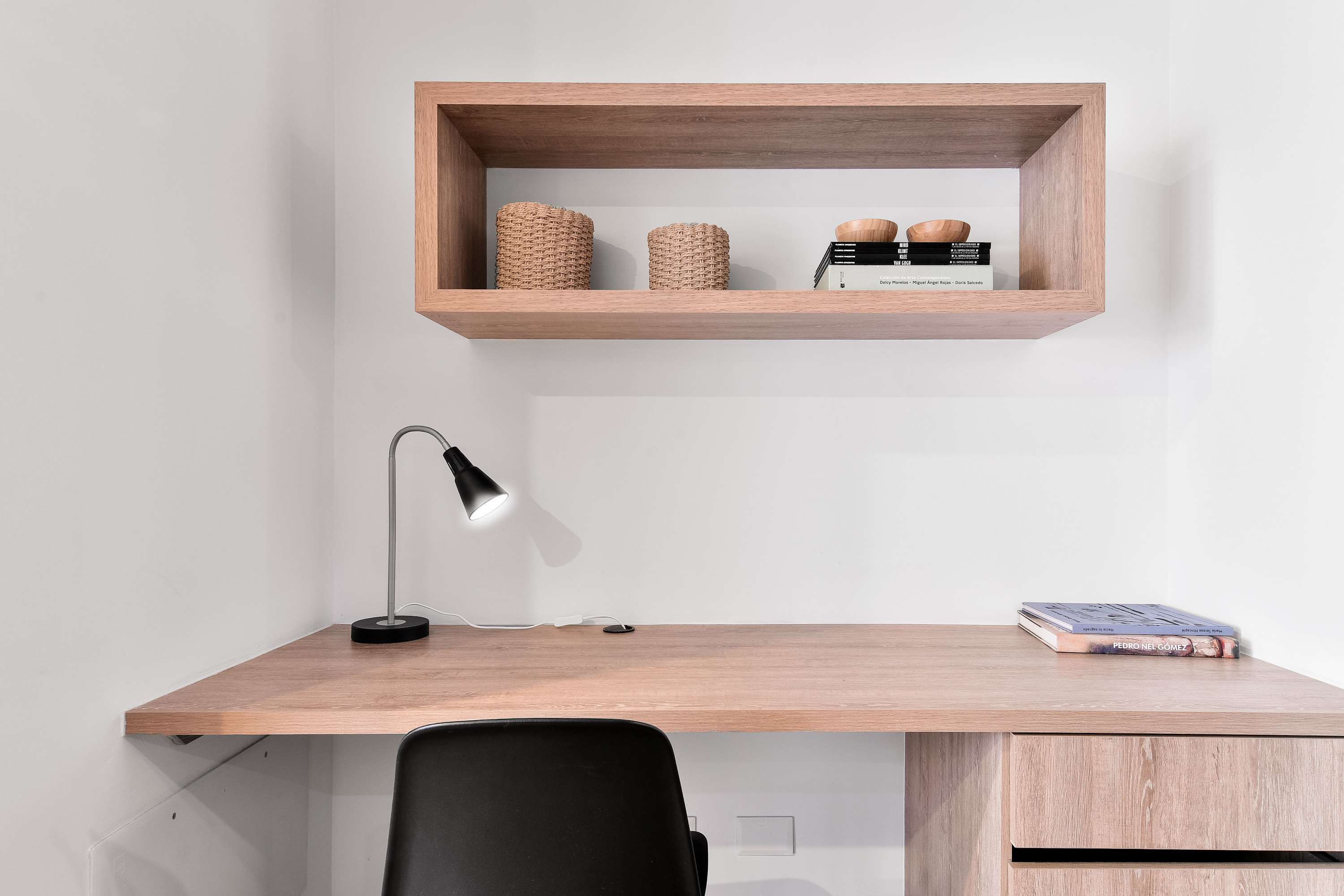 Un escritorio de madera con un estante superior que contiene dos cestas tejidas y una pila de libros.