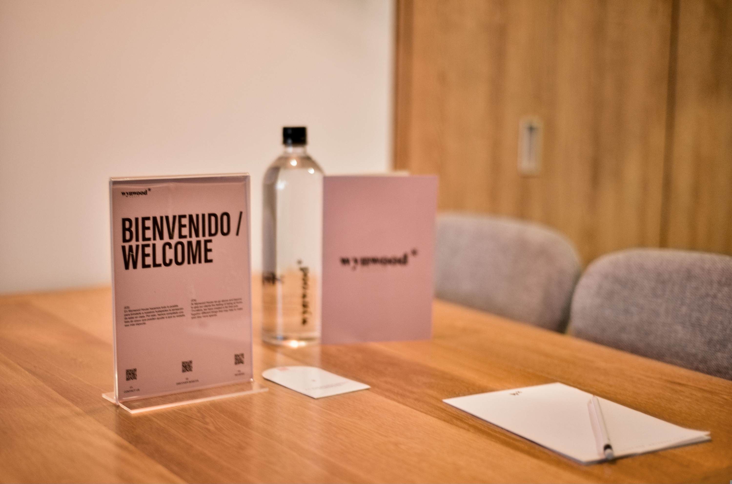 Een houten tafel met een bordje welkom, een fles en een notitieboekje.