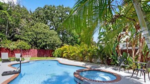 Ein Garten mit Swimmingpool, umgeben von einem Holzzaun, Palmen und einer Pflasterterrasse.