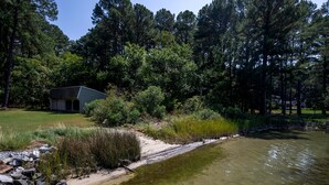 A pond with a wooden dock, surrounded by dense trees and a small building. - Minutes from Downtown St. Michaels | Private Boat Ramp | Dock (Bozman)