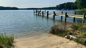 A sandy beach with a wooden pier extending into calm water, surrounded by greenery. - Minutes from Downtown St. Michaels | Private Boat Ramp | Dock (Bozman)