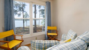A room with a large window overlooking a lake, a yellow folding chair, a plaid sofa, and a modern ceiling light fixture. - Minutes from Downtown St. Michaels | Private Boat Ramp | Dock (Bozman)