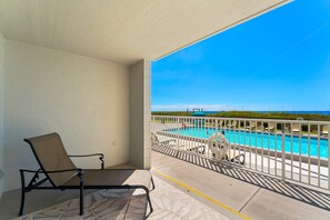 A balcony with a view of a swimming pool, a lounge chair, and a railing. - FREE Golf & Perks! Mariner West 103, Walk-In Shower, Gulf Front Pool & Grill! (Panama City Beach)