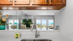 Una cocina con un lavamanos doble, armarios de madera y vistas a la piscina y la playa.