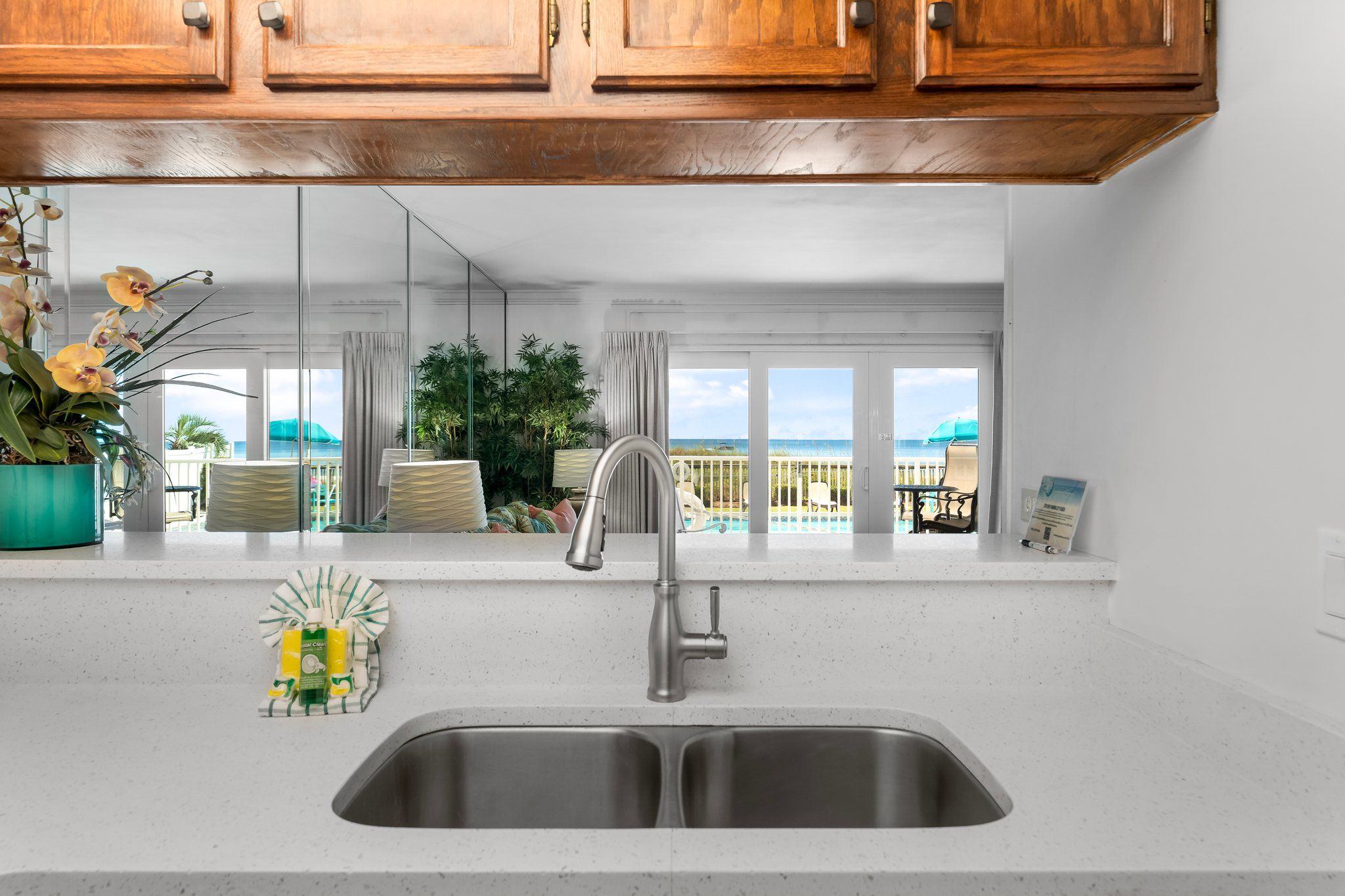 Una cocina con un lavamanos doble, armarios de madera y vistas a la piscina y la playa.