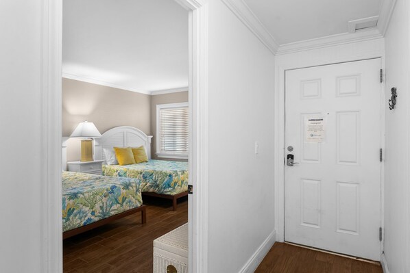 A bedroom with two beds, a nightstand, a lamp, and a door with a sign.