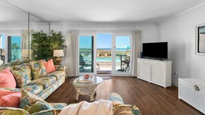 Un salón con sofá, una mesa de centro de vidrio, televisor y balcón con vista a la piscina.