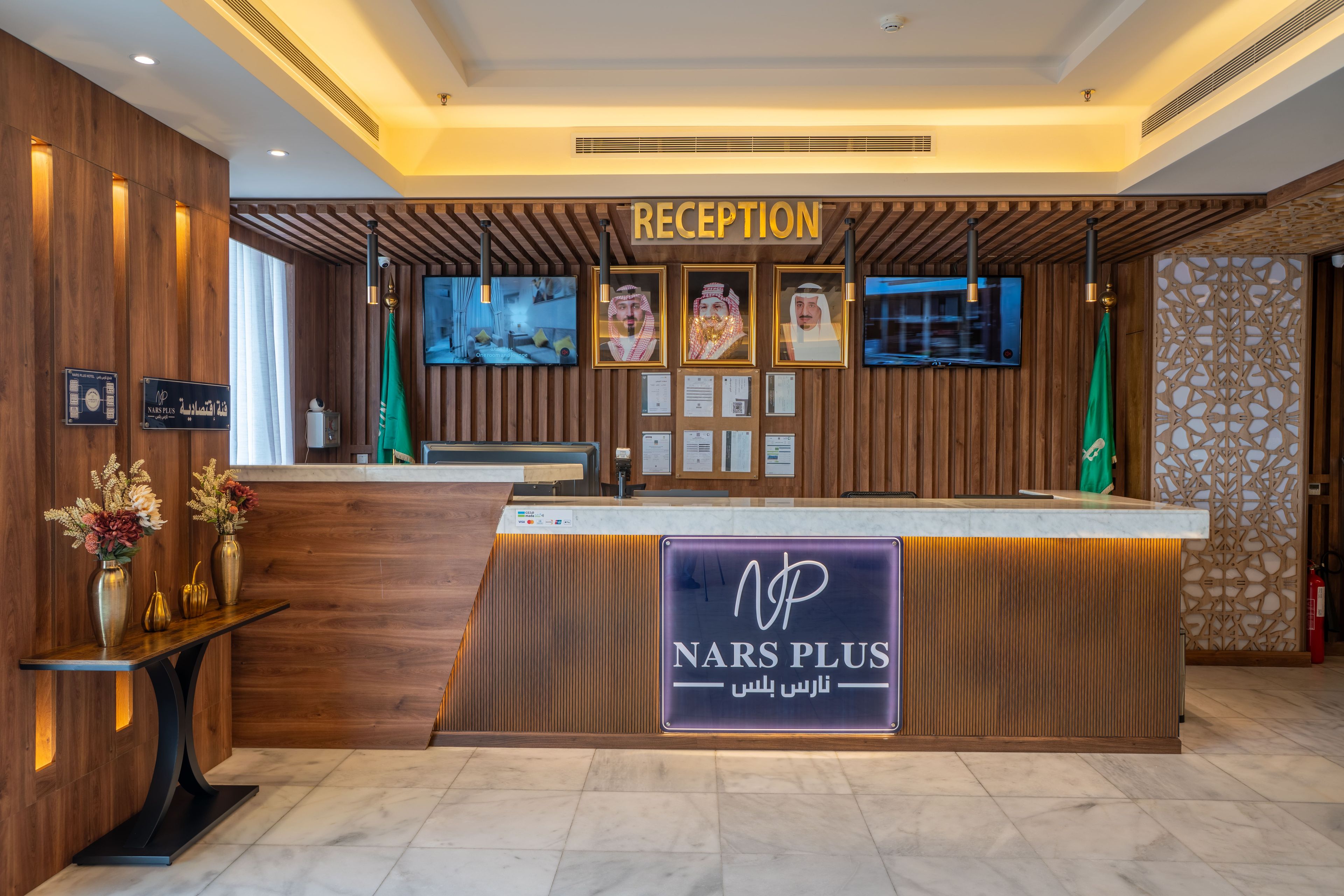 Un mostrador de recepción con un letrero 'NARS PLUS', certificados enmarcados y una pantalla de televisión.