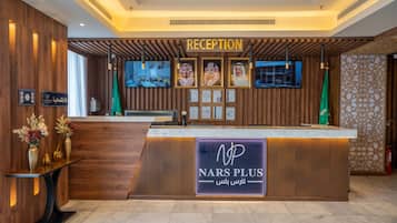 Un taulell de recepció amb un cartell de 'NARS PLUS', diplomes emmarcades i una pantalla de televisió.