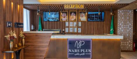 Un mostrador de recepción con un letrero 'NARS PLUS', certificados enmarcados y una pantalla de televisión.