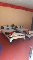 Habitación de hotel con dos camas, cada una con una colcha de motivos florales, una mesita con un jarrón y un suelo cubierto de alfombra roja.
