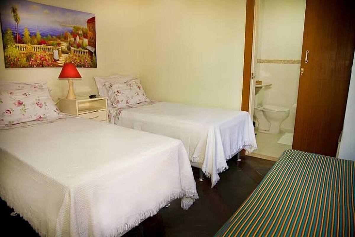 Quarto de hotel com duas camas, um quadro na parede e banheiro visível através de uma porta aberta.