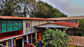 A multi-story building with a red roof, large windows, and a balcony. - KUMBH GANGA RETREAT (Karchana)