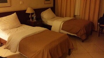 Habitación de hotel con dos camas, una mesita de noche con lámpara y una silla.