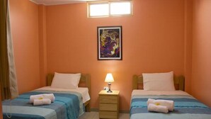 A room with two beds, a nightstand with a lamp, and a painting on the wall. - KUMBH GANGA RETREAT (Karchana)