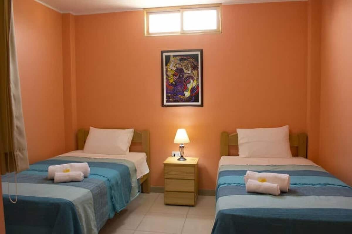 Quarto com duas camas, uma mesa de cabeceira com abajur e um quadro na parede.