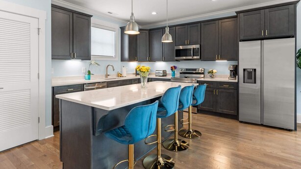 A modern kitchen with dark cabinets, a large island with blue bar stools, stainless steel appliances, and pendant lighting. - Chic Townhome for 8 w/Rooftop (Nashville)