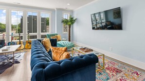 A living room with a blue sofa, a green armchair, a coffee table, and a TV mounted on the wall. - Chic Townhome for 8 w/Rooftop (Nashville)