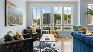A modern living room with a large window, a black leather sofa, a blue sofa, and a coffee table. - Chic Townhome for 8 w/Rooftop (Nashville)