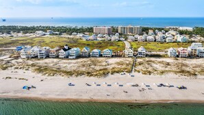 Vue aérienne d’une station balnéaire avec des villas en bord de mer, une promenade en bord de plage et un port de plaisance.
