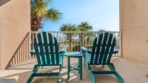 Un balcon avec deux fauteuils Adirondack verts et une petite table, d’où l’on peut admirer des palmiers et un ciel dégagé.