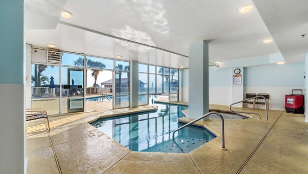 Une piscine intérieure avec des parois en verre transparent, un sol carrelé et un escalier pour accéder au bassin.