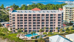 Un hôtel à plusieurs étages doté d’une piscine, situé près d’une plage et d’un port de plaisance.