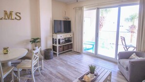 Un salon comprenant un téléviseur, une table à manger, des chaises, un canapé et une porte-fenêtre coulissante donnant sur un espace extérieur.