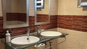 A bathroom with two sinks, a glass countertop, a mirror, and a towel dispenser.
