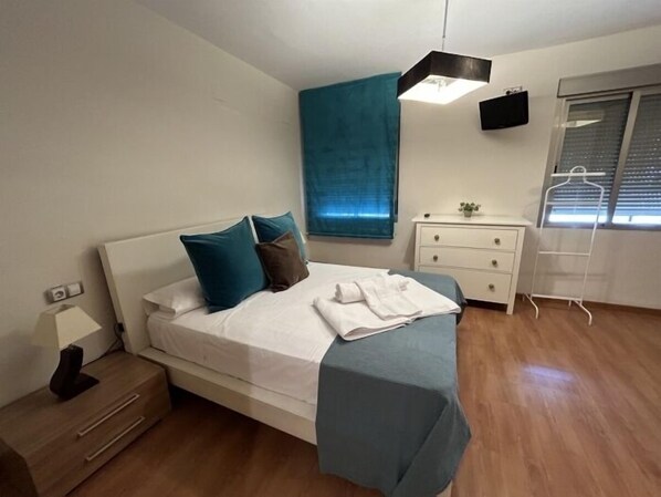 Un dormitorio con cama, mesita de noche, cómoda y una ventana con persianas.