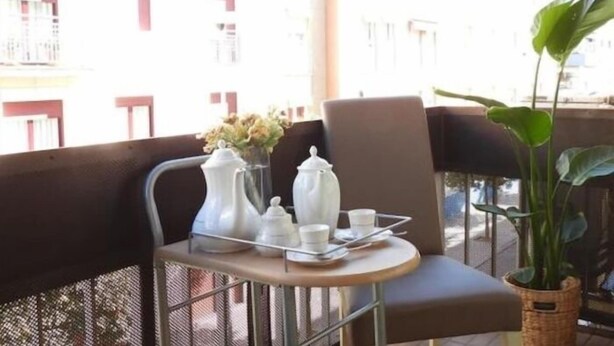 A balcony with a table set for tea, a chair, and a potted plant.