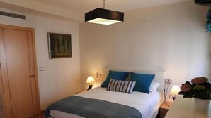 A bedroom with a bed, bedside lamps, a painting on the wall, and a door.