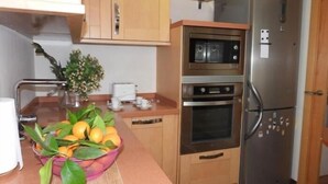 A compact kitchen with wooden cabinets, a stainless steel refrigerator, a built-in oven, and a microwave.