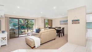 Relax in this serene space with a beige sofa, dining table, and sliding glass door leading to a lush outdoor area.