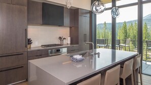 Eine moderne Küche mit einer großen Kochinsel, Edelstahlgeräten und Blick auf einen Balkon mit Sitzgelegenheit.