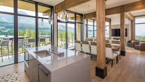 Eine moderne Küche mit einer großen Kochinsel, Essbereich mit Stühlen und Bergblick durch große Fenster.