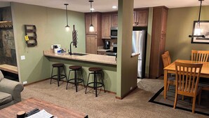 Una cocina compacta con una isla central, taburetes de bar, armarios de madera y una zona de comedor con mesa y sillas.