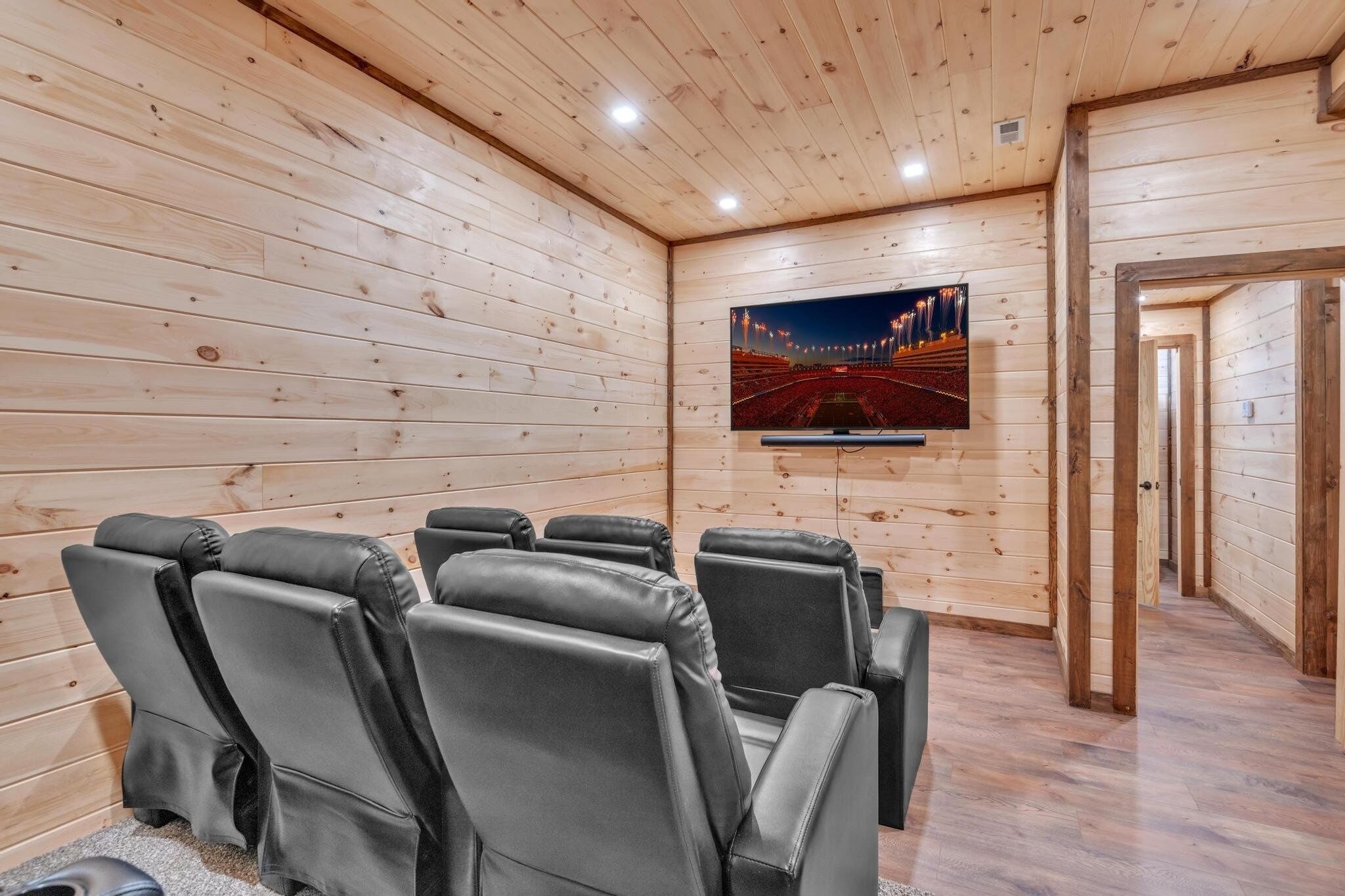 A wooden-paneled room with a flat-screen TV mounted on the wall, leather reclining chairs, and a carpeted floor.