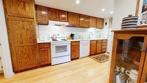 Une cuisine avec des meubles en bois, des appareils électroménagers blancs et un meuble vitré contenant des objets décoratifs.