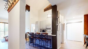 A modern kitchen with bar stools, a dining area with a wooden table, and a view of the outdoors.