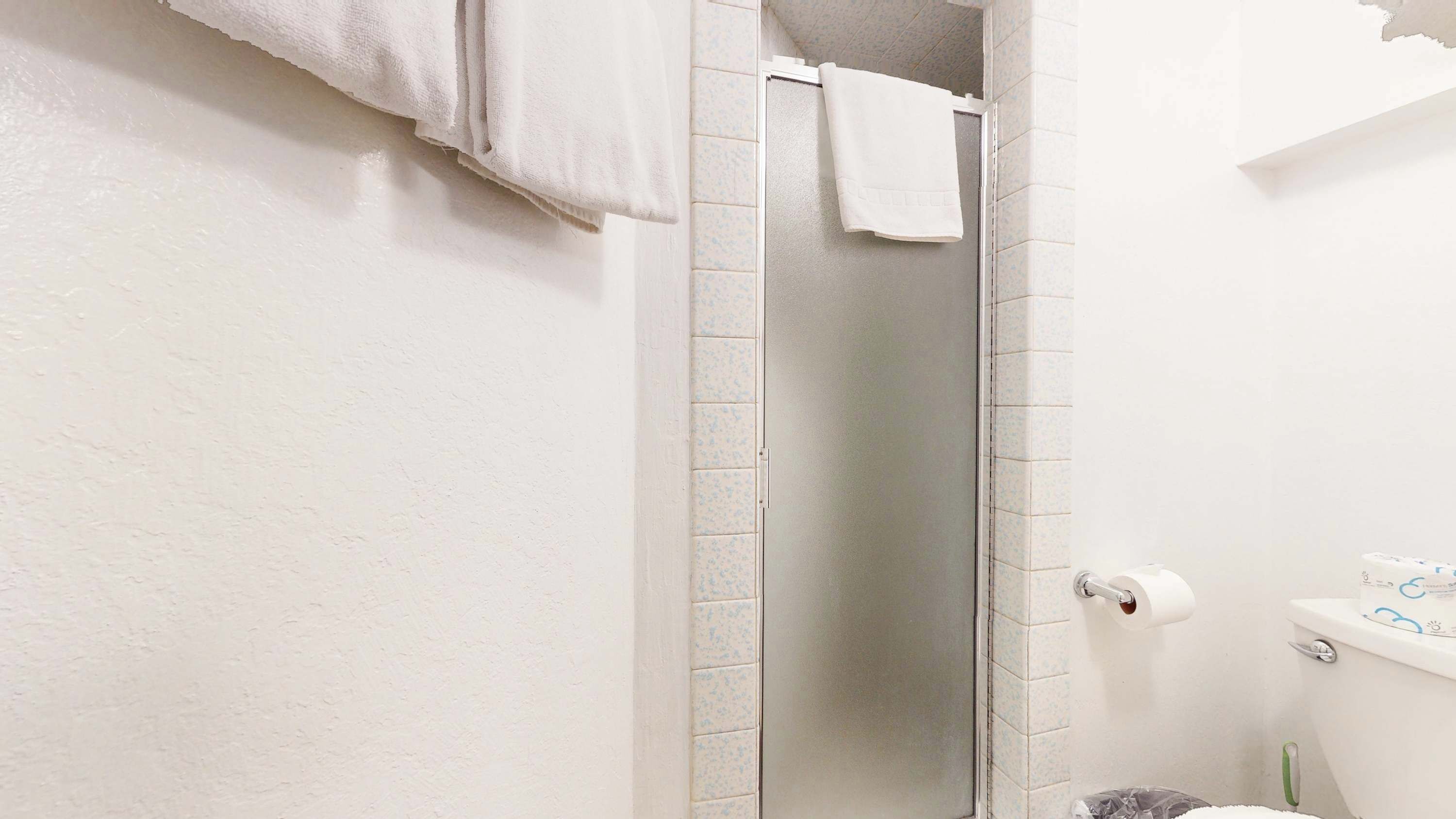 Un baño con ducha, paredes blancas y un inodoro.