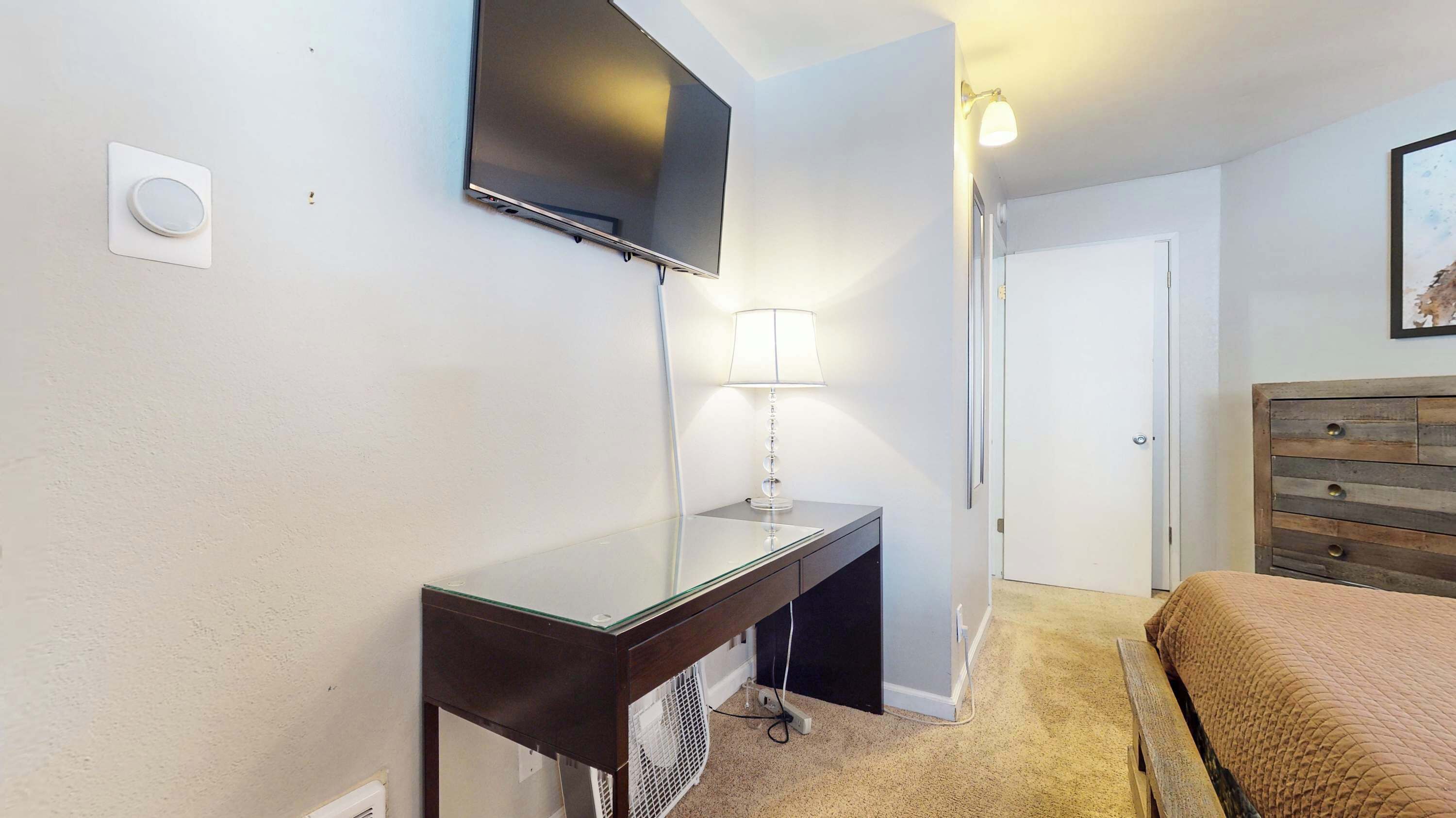 Hotelkamer met een flatscreen televisie aan de muur, een nachtkastje met lamp, een houten hoofdbord en een deur.