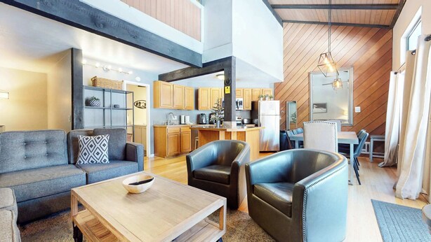 A spacious living area with a sofa, armchairs, and a coffee table. A kitchen is visible in the background with wooden cabinets and modern appliances.