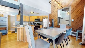 A modern kitchen with wooden cabinets, a stainless steel refrigerator, and a dining area with a large table and chairs.