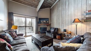 A cozy living room with a fireplace, a large TV, and a sign indicating nearby locations like a village, canyon, and lakes.
