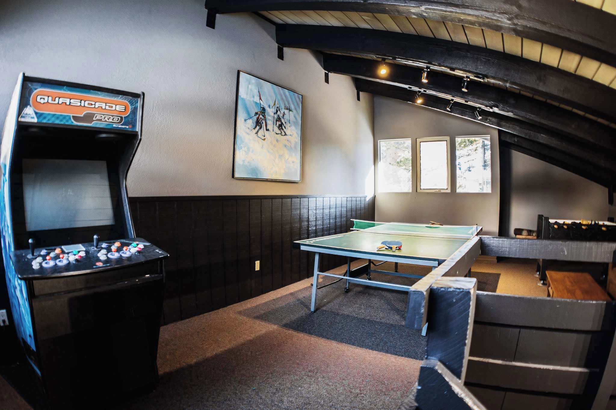 Een kamer met een tafelvoetbaltafel, een pingpongtafel en een tafeltennistafel. Er hangt een schilderij aan de muur en de tafelvoetbaltafel is gemarkeerd met 'Quasicade Pro'.